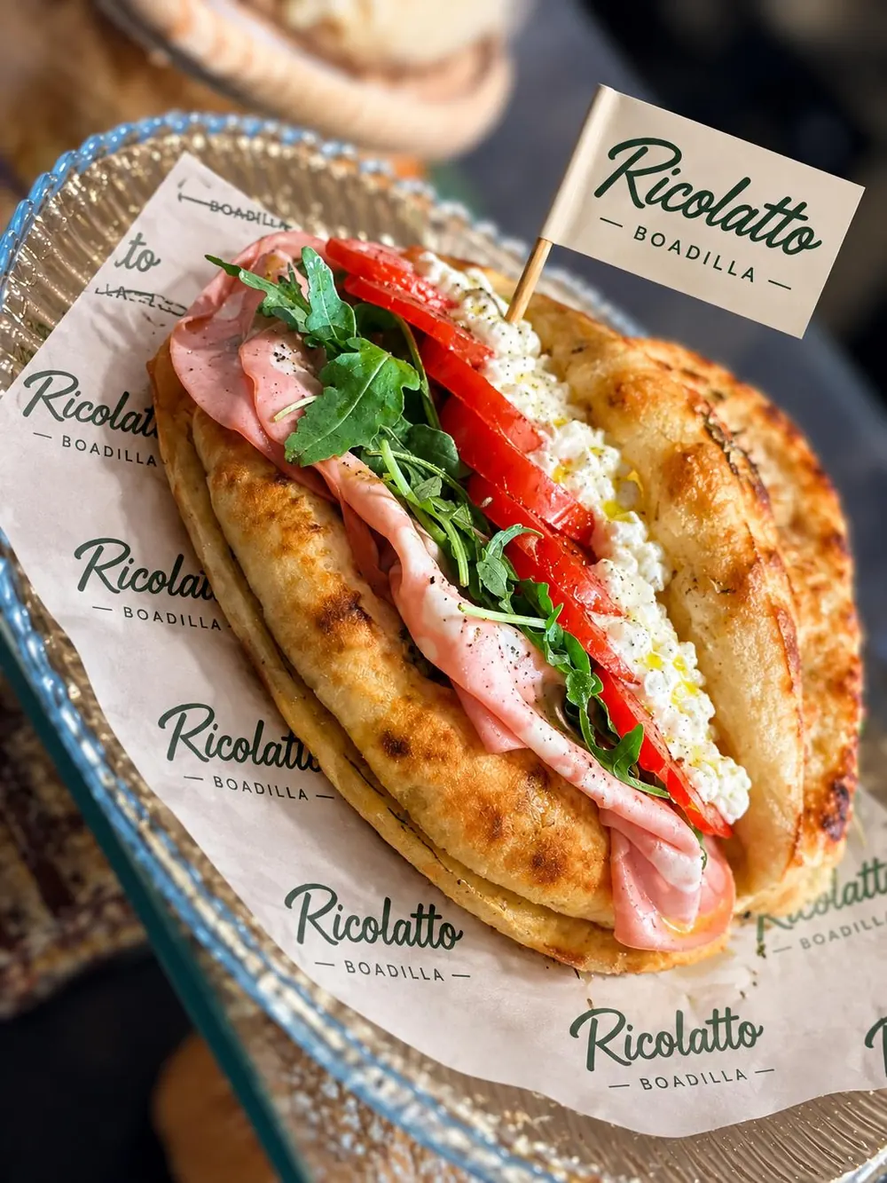 Bocadillo de pan plano con jamón, rúcula, pimiento y queso fresco