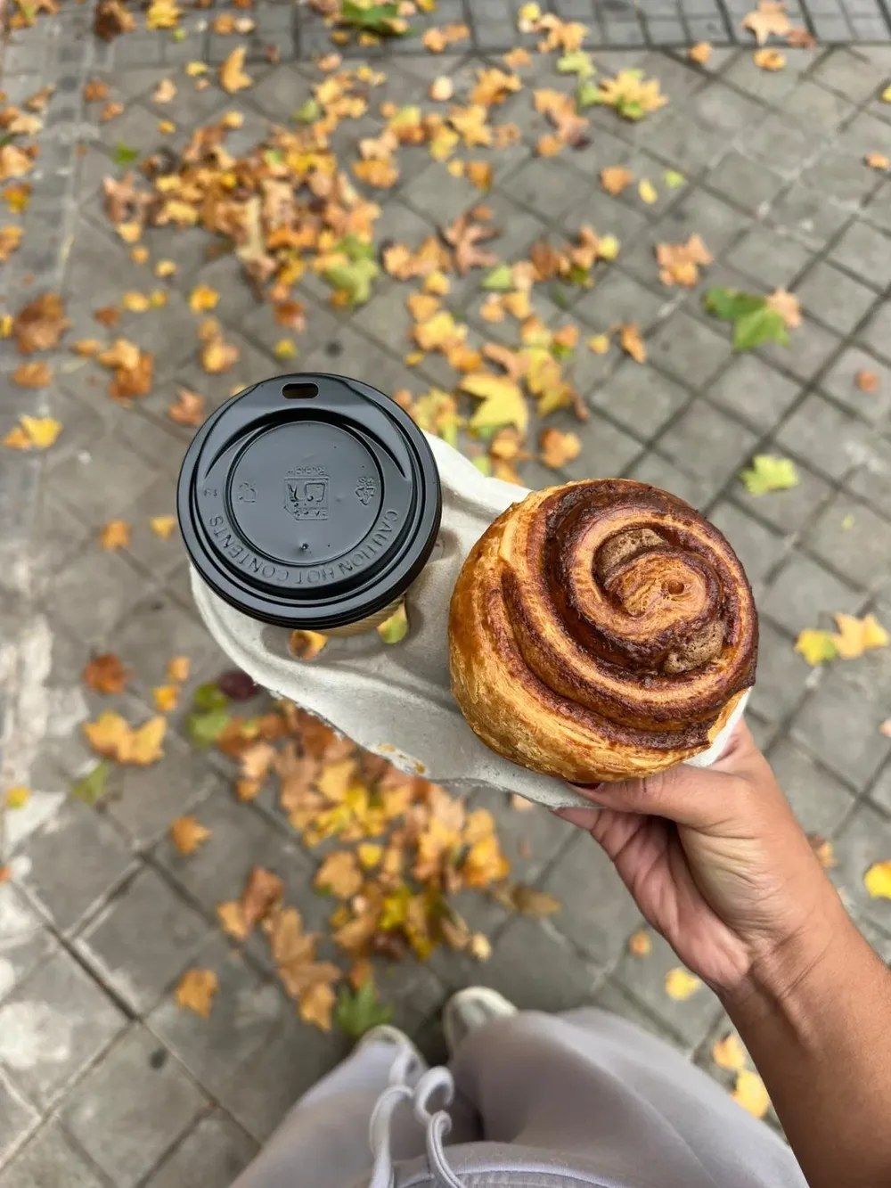 Napolitana de hojaldre y café para llevar en una bandeja de cartón, sobre un suelo de hojas de otoño
