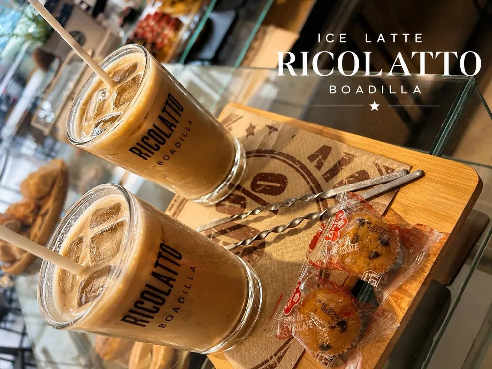 Dos ice lattes de Ricolatto con hielo y pajitas sobre una tabla de madera, con dos magdalenas de chocolate