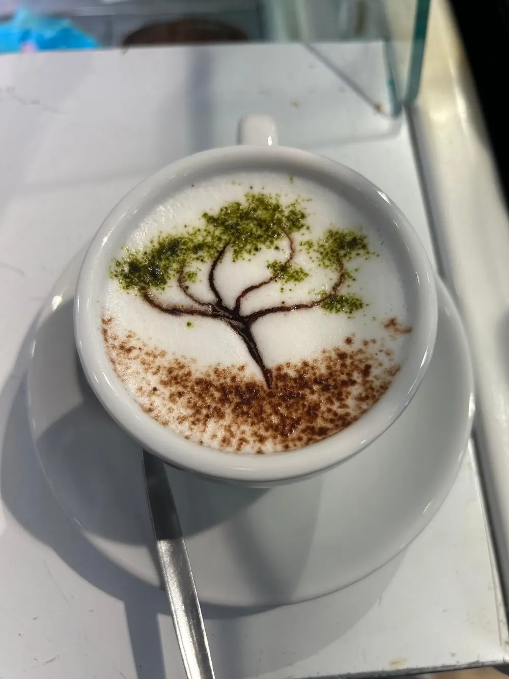Capuchino con un árbol dibujado en la espuma con cacao y matcha