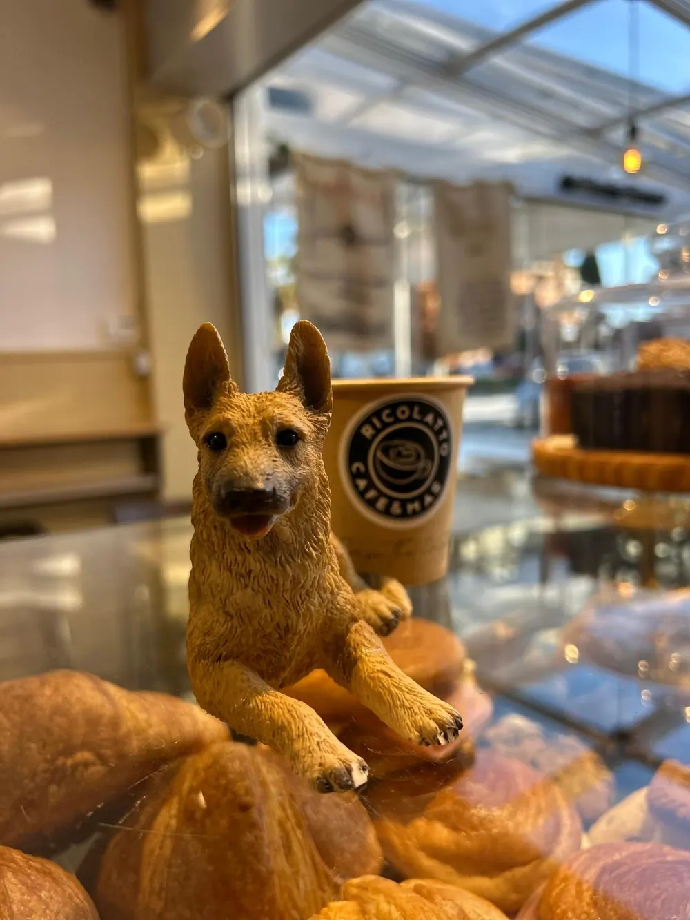 Figura de un perro sobre la vitrina de bollería, junto a un vaso de Ricolatto