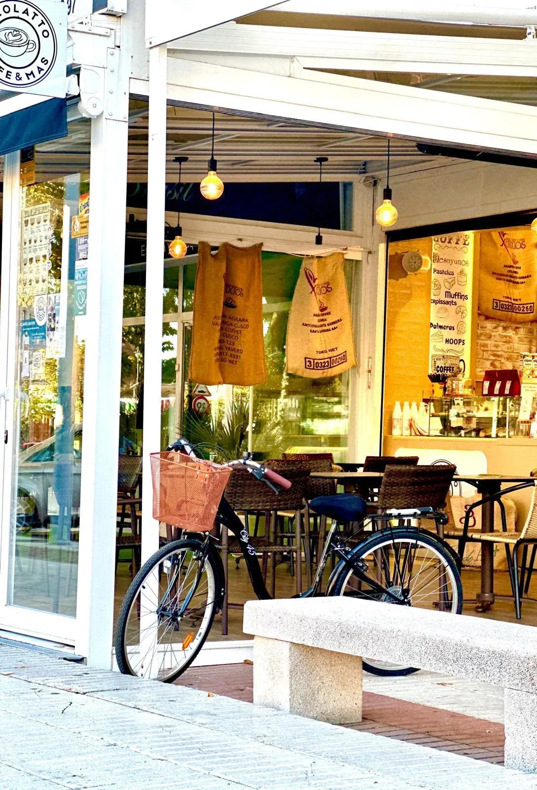 Entrada de Ricolatto con la terraza, sacos de café colgados, una bicicleta y un banco de piedra